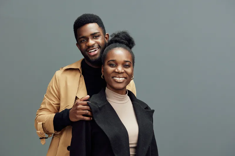 Stylish young couple smiling joyfully against a neutral background, showcasing modern fashion and happy emotions, perfect for lifestyle and relationship themes