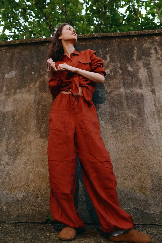 Woman in rust jumpsuit standing against a textured wall outdoors, displaying casual chic and confident urban lifestyle, with natural light soft light adding warmth