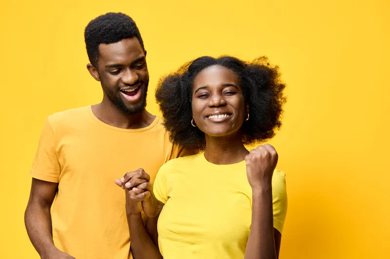 Happy young couple celebrating success in matching outfits against a vibrant yellow background, expressing joy and love