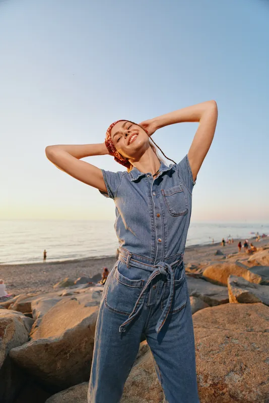 lifestyle woman in modern boho-western denim street style enjoying sunset by the beach with relaxed joyful expression in warm film color tones