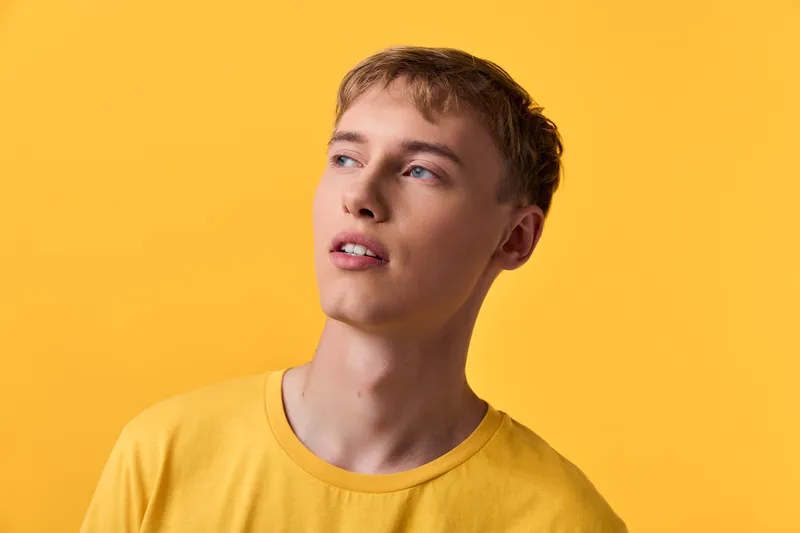 Man wearing a yellow shirt gazes upward against a bright yellow backdrop, conveying a thoughtful, modern mood for fashion and lifestyle visuals with clean lines and warm tones.