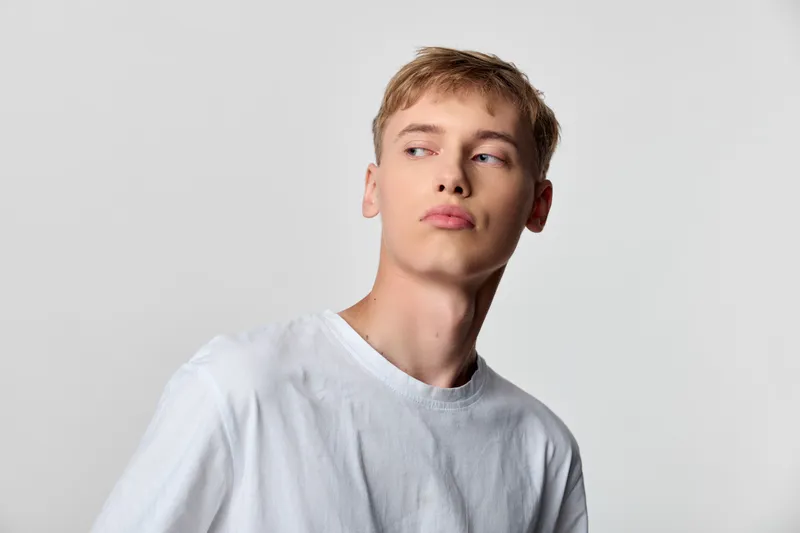 Youth model with a contemplative profile wearing a white shirt in a clean studio, evoking calm fashion and modern minimalism for lifestyle and editorial use