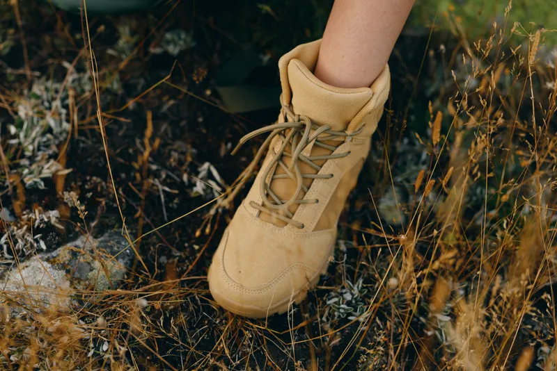 Close up of a tan boot stepping through dry grass in an outdoor setting, showcasing natural textures, earthy tones and a casual lifestyle moment outdoors