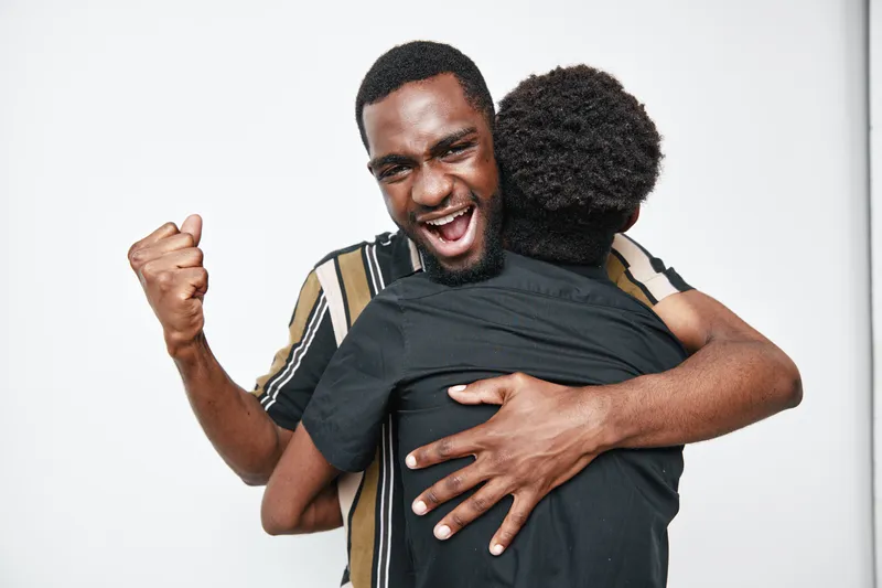 African American man with dark skin celebrating and hugging child with curly hair in casual clothes on white background for family and happiness.
