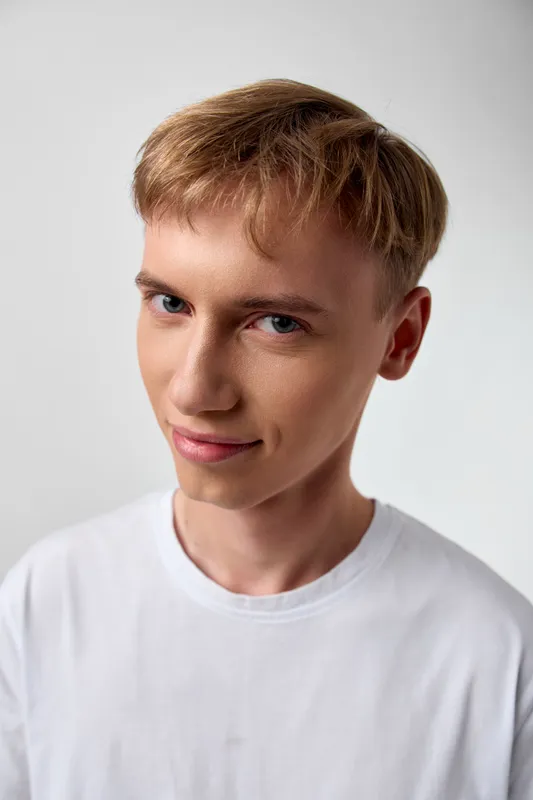 Man in a white t shirt with a gentle smile, head tilt, photographed in a studio with a neutral background for a clean, versatile headshot style