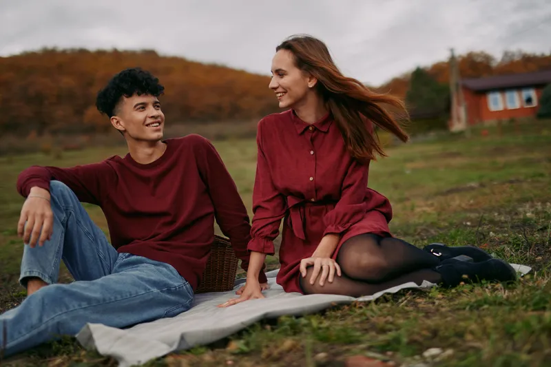 Young couple sitting on a blanket in the countryside sharing a warm moment during an autumn picnic, a genuine candid portrait capturing natural smiles, honest connection and simple everyday intimacy.