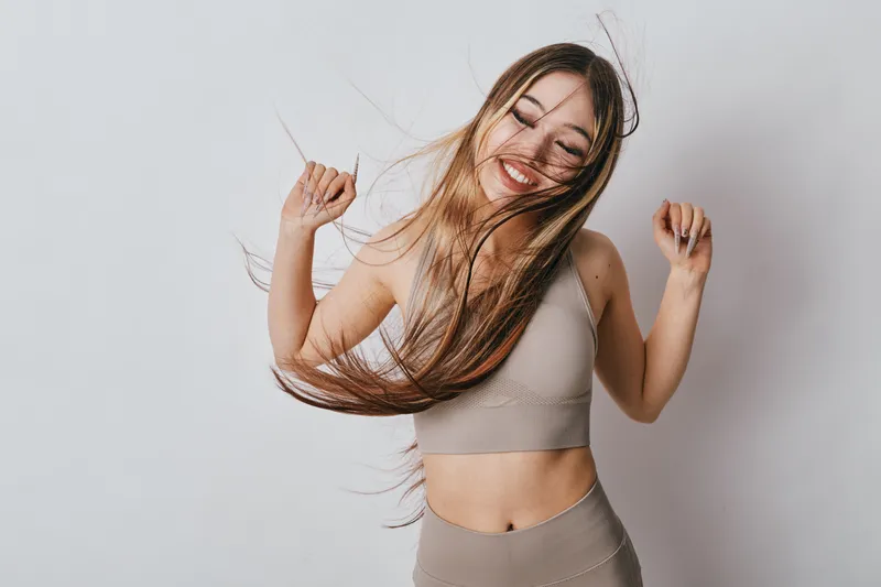 Young woman smiling and dancing with long hair in sportswear against plain background. Fitness, joy and active lifestyle with happy female enjoying movement and health.