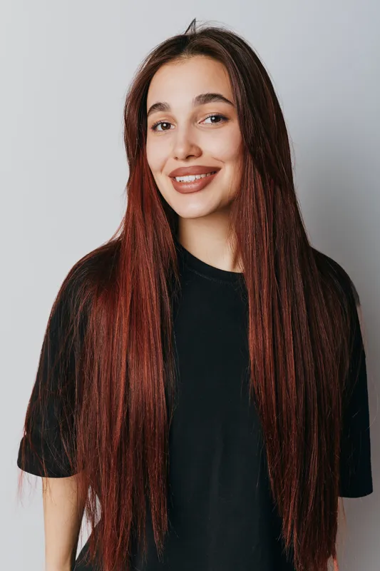Young woman with long straight brown hair smiling and posing in black t shirt on light gray background. Casual style, beauty, portrait and happiness with natural makeup and confident look.