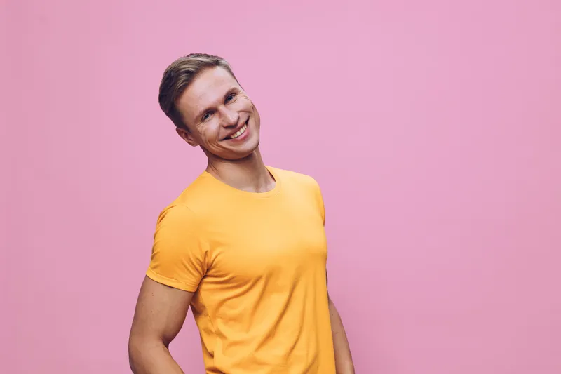 Smiling man in bright yellow t-shirt posing against pink background, cheerful expression, casual style, studio shot, vibrant colors, lifestyle concept, positive emotion