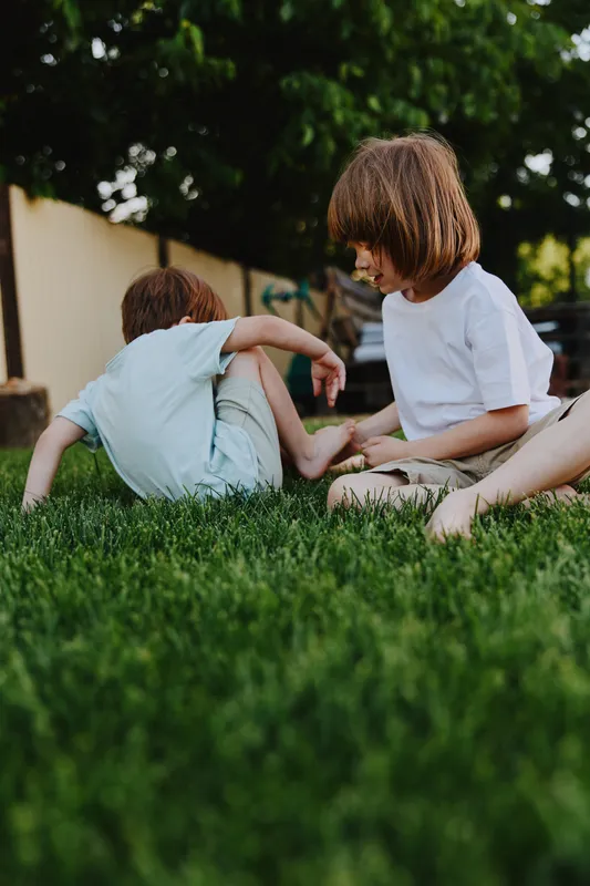 Two playful children engaged in outdoor play, enjoying the green grass on a sunny day. Their laughter adds to the joyful atmosphere of childhood fun.