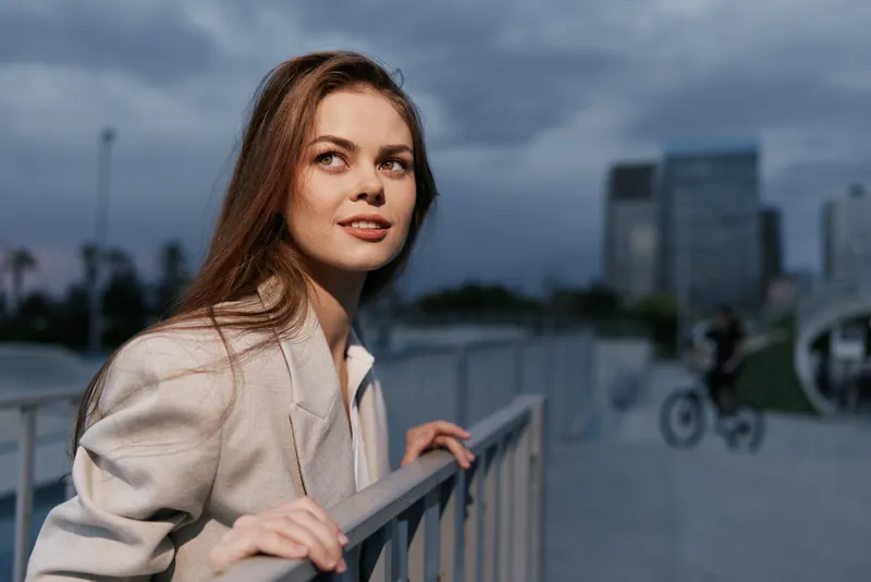 Young businesswoman smiling outdoors in a sleek suit, showcasing confidence against a modern urban backdrop with a dynamic color palette.