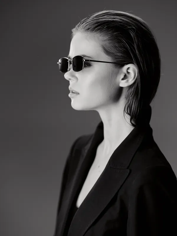 Black and white portrait of a stylish woman wearing sunglasses and a blazer with a serious expression