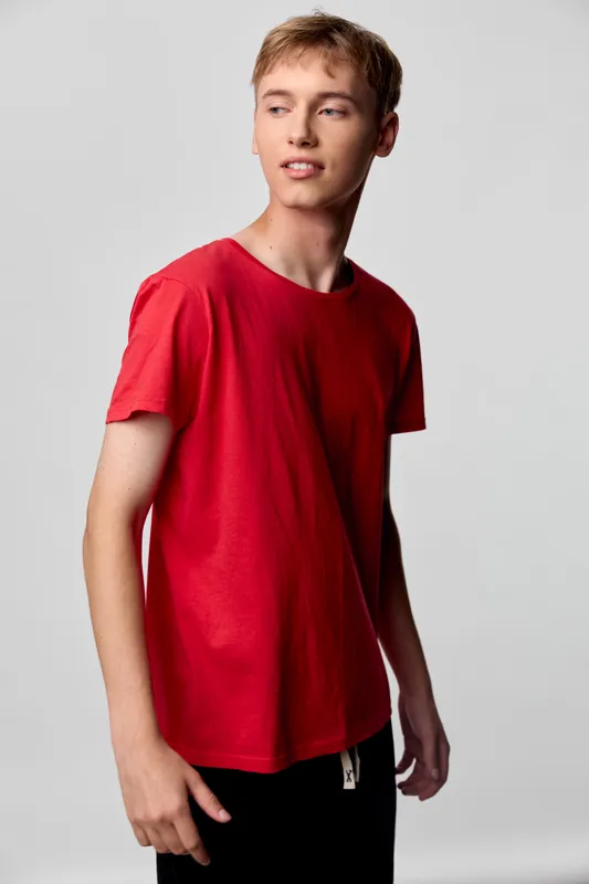 A red shirt worn by a male model in a studio shoot, showcasing casual fashion and youthful style with a minimal background in a clean studio.