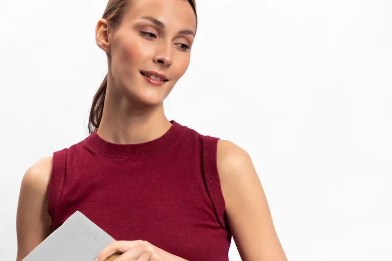 Young woman in sleeveless red top looks down with slight smile holding a tablet. Isolated on white background. Concept for technology, education, and casual lifestyle.