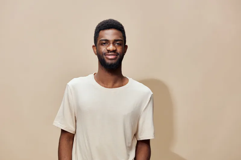 Young Black man smiling in a light beige t shirt against a soft neutral background exuding confidence and warmth