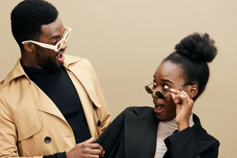 Two surprised young models showcase trendy sunglasses against a neutral beige background, reflecting a playful, modern fashion concept perfect for advertising