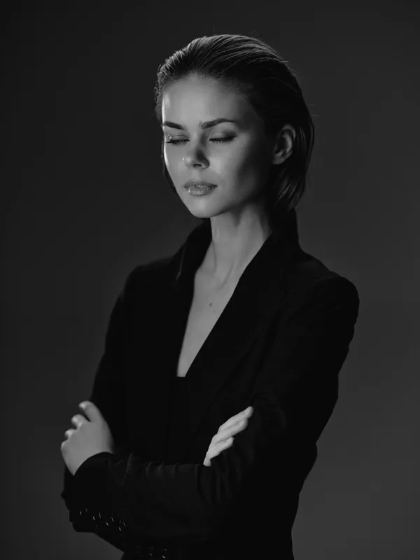 Thoughtful woman with closed eyes in black blazer, monochrome portrait with soft lighting and calm expression.