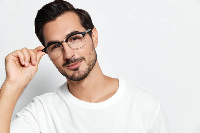 Young smiling man wearing glasses, casual white t-shirt, looking at the camera with a charming expression, isolated on solid light background. Stylish portrait concept.