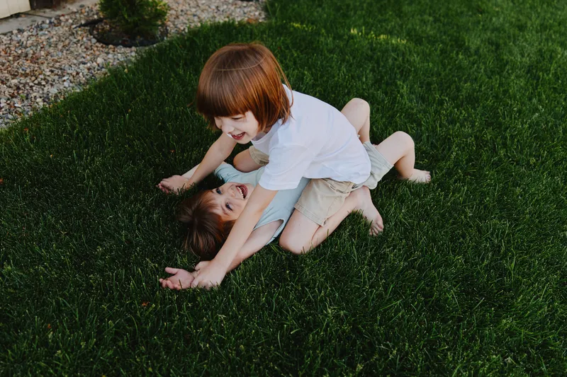 Two children playing happily outdoors on green grass, enjoying a sunny day in a playful atmosphere, expressing joy and innocence in their carefree moment.