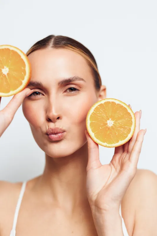 Woman holds orange citrus slices by cheeks for natural skincare beauty, fresh healthy spa concept, vitamin c hydration and glow on isolated portrait, studio light on white background