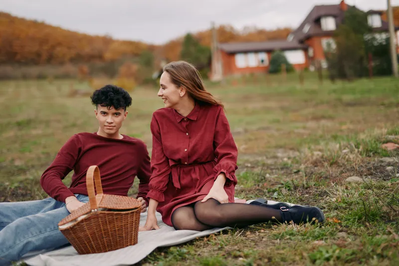 A candid outdoor portrait of a young couple enjoying a rustic autumn picnic on a blanket, capturing authenticity and natural expressions with credible, unposed interaction in a serene countryside