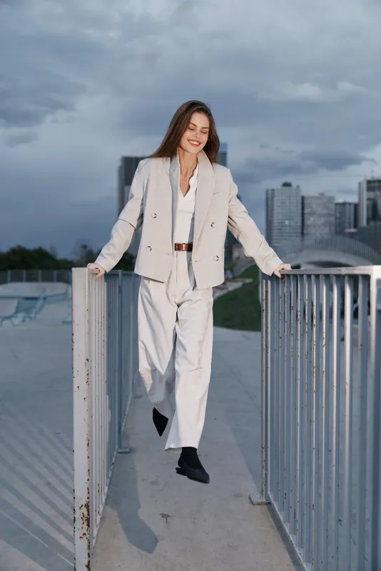 Young woman in light suit walking confidently outdoors with urban background during cloudy day fashion business style