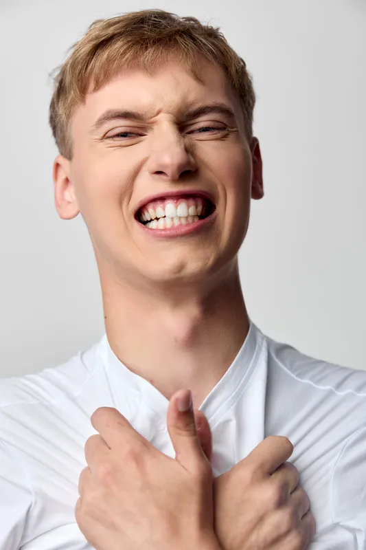 Smiling man with raised thumbs and clenched fists, expressing excitement and energy, close up shot capturing a joyful, triumphant moment in a simple studio setting with bright lighting and neutral
