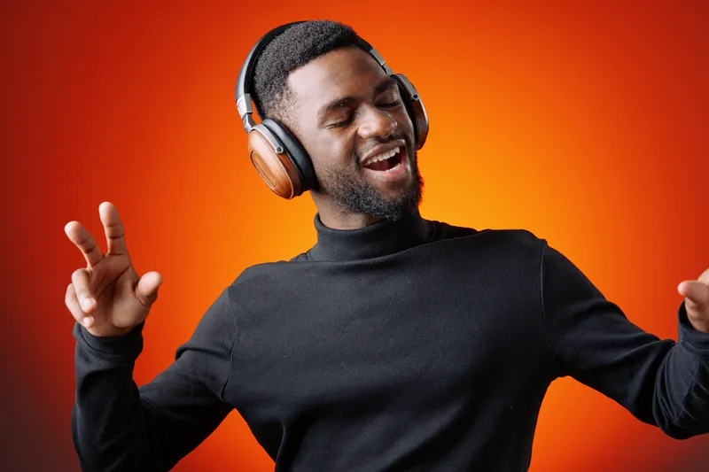 Young African American man enjoying music with headphones, smiling with joy against a vibrant orange background, ideal for music and lifestyle themes