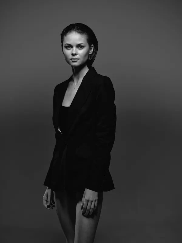 Black and white portrait of a young woman in dark clothing with a serious expression and minimalist background.