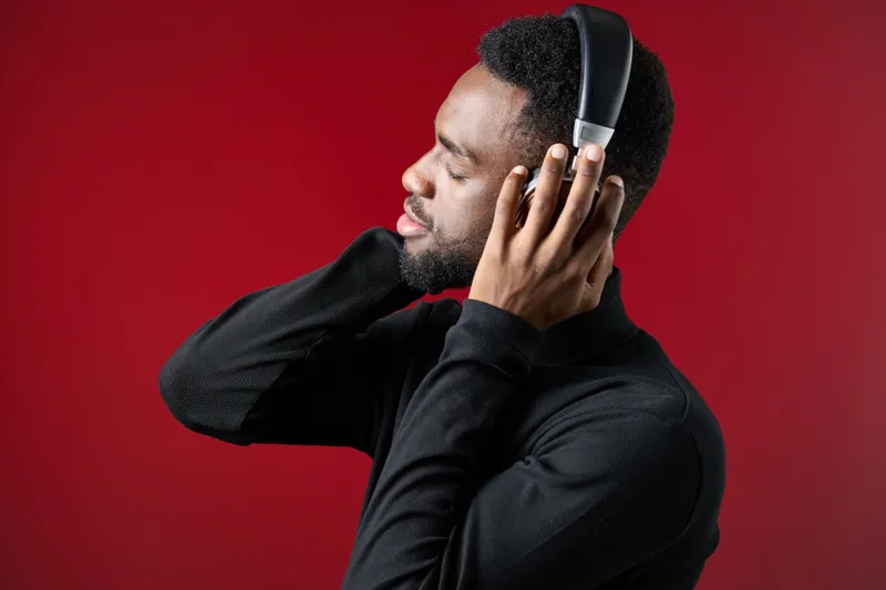 Young Black man enjoying music with headphones, expressing joy and relaxation against a vibrant red background