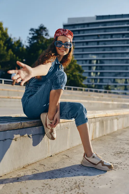 Lifestyle woman in modern boho-western denim street style wearing sunglasses and a red bandana, captured with vibrant film color in an urban outdoor setting.