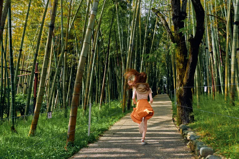 girl bamboo path running in a green forest, back view of a barefoot child in orange skirt on a sunlit trail, motion and freedom in nature during summer outdoors exploration.