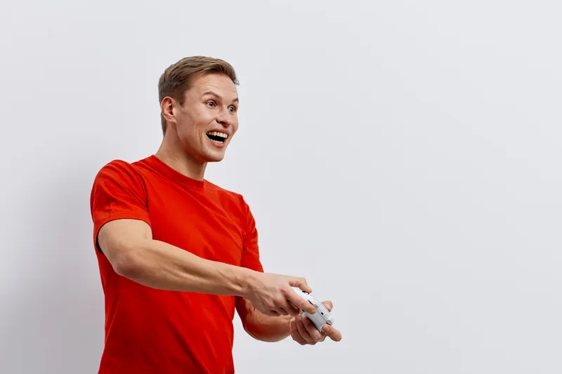 excited young caucasian man in red t-shirt holding wireless game controller playing video games isolated on white background digital entertainment concept