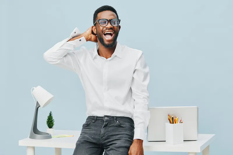 Smiling man wearing white shirt and glasses, standing in modern office with light blue background, cheerful expression, casual pose, during daytime. People lifestyle concept, professional, happy, rela