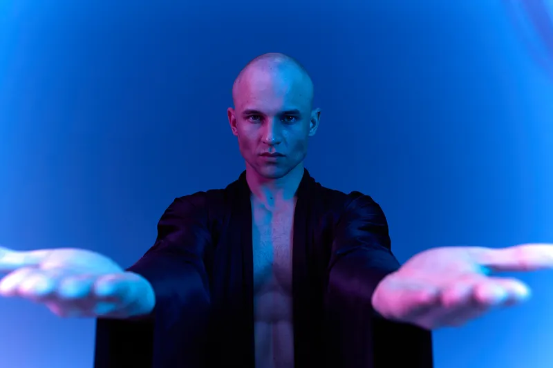 Man in a dark robe with outstretched hands, illuminated by vibrant blue light. A striking aura creates a sense of mystery and engagement in this captivating scene.