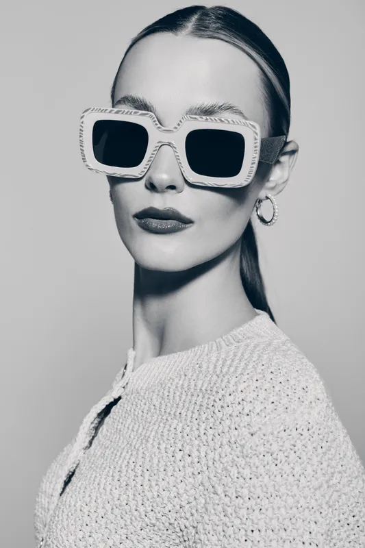 Stylish white woman with pale skin wears large sunglasses and hoop earrings. Monochrome portrait with serious facial expression and trendy fashion.