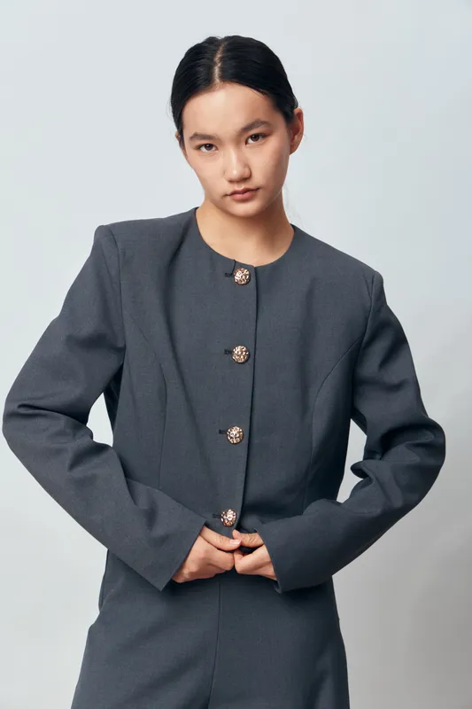 Young woman wearing dark gray buttoned jacket posing on light background with serious expression, stylish minimalist outfit for fashion and casual portrait concept.
