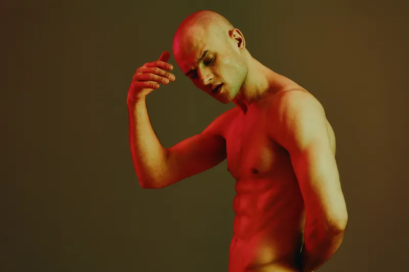 Thoughtful man in a striking pose, featuring a blend of warm red tones and a minimalist backdrop. The focus on emotion adds depth to the scene.