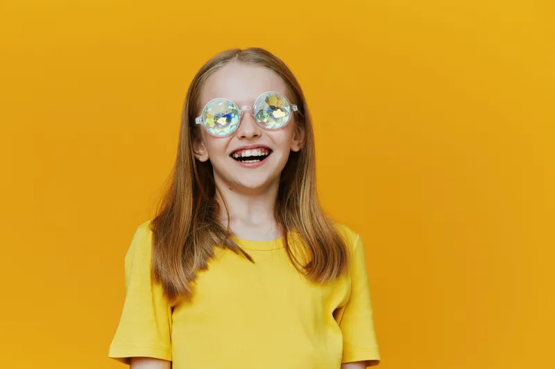 Cheerful girl with long hair wearing a yellow t shirt and colorful sunglasses against a bright yellow background, radiating joy and positivity, perfect for summer themes