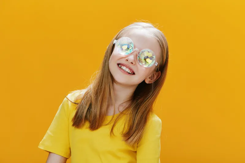 Happy young girl with long hair in yellow shirt and stylish sunglasses on a vibrant yellow background, embodying joy and summer fun