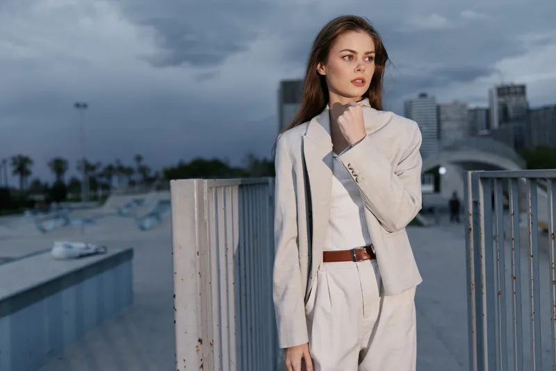 Confident woman in a light business suit against a modern cityscape, showcasing a professional and elegant demeanor, perfect for corporate contexts.