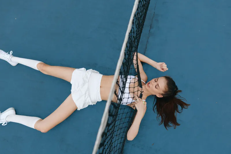 Young woman exhausted on a tennis court, displaying emotions of fatigue and determination, wearing sporty attire, illustrating the challenge of athletic performance in vibrant colors