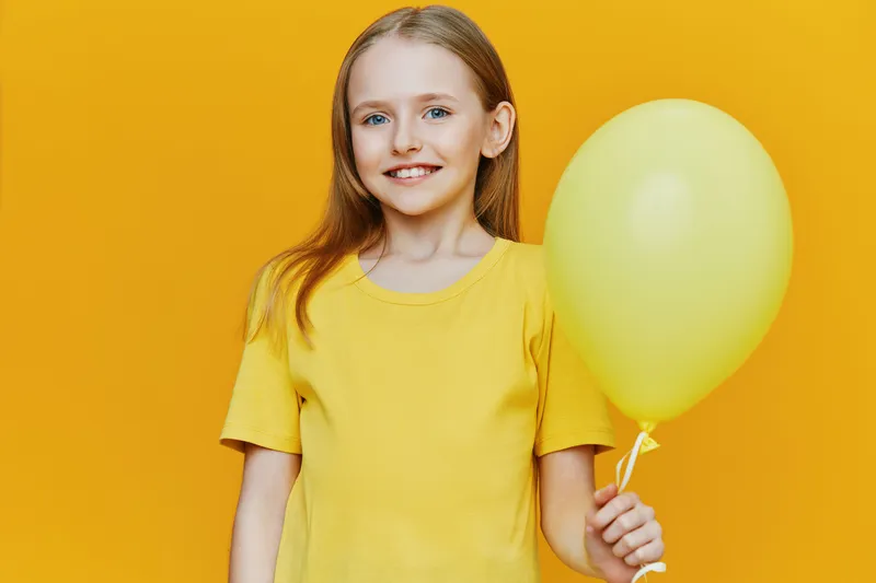 Happy girl holding a yellow balloon, wearing a bright yellow t shirt, smiling against a vibrant yellow background, perfect for cheerful and playful concepts