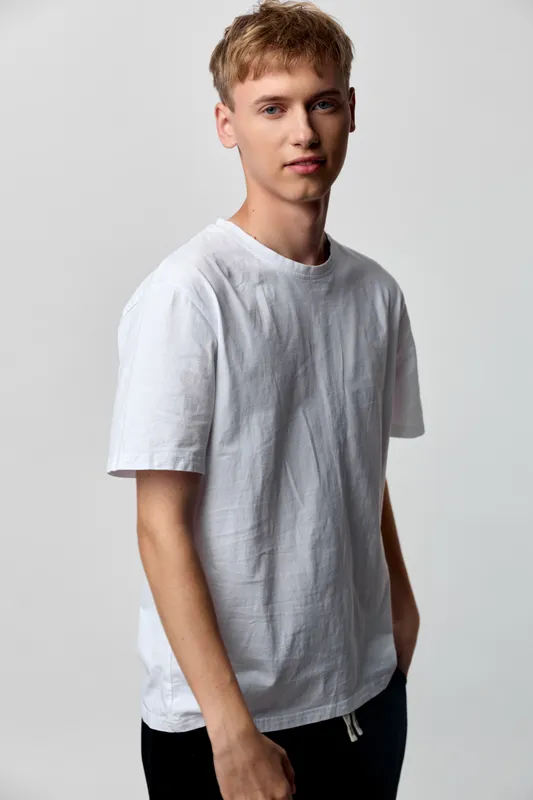 Young man in a white tshirt stands in a neutral studio setting with relaxed posture and confident expression, delivering a clean casual look ideal for lifestyle or product style imagery