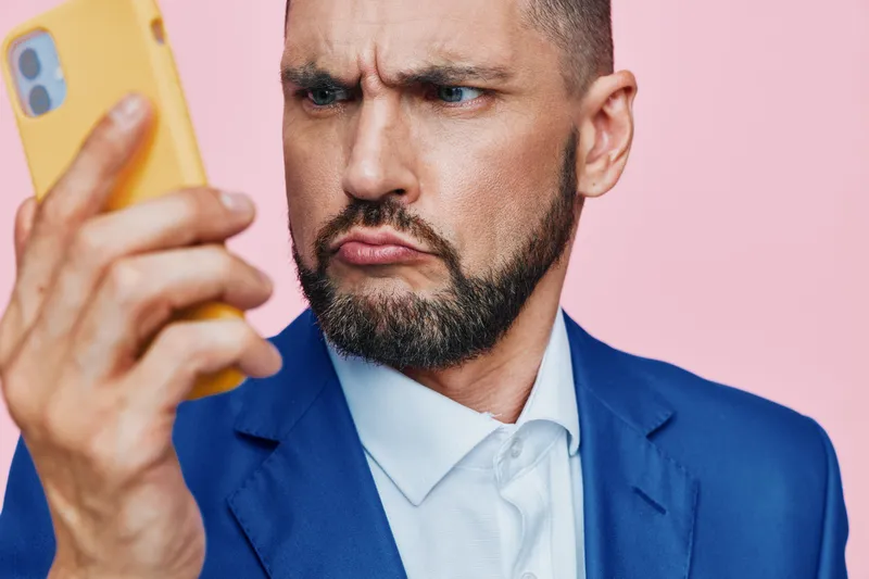 A professional man in a blue suit gazes at a smartphone, set against an isolated colorful backdrop. The portrait conveys focus, confidence, and determination in a business context.