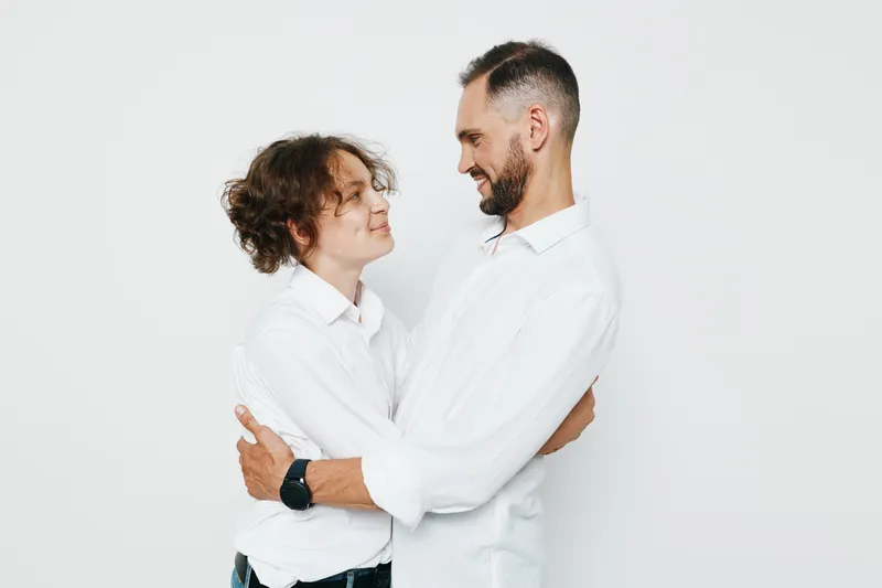 A professional man in a white shirt stands with a colleague against a clean solid background, conveying confidence, teamwork, and positive emotion in a business setting.