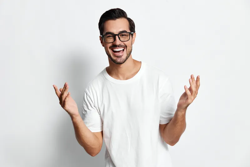 Full body cheerful smiling man in white t-shirt looking at camera with excitement and open hands, isolated on plain light background. People lifestyle concept.