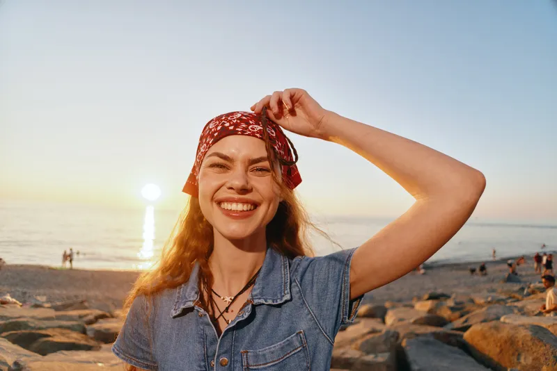 smiling woman wearing denim jacket and red bandana on beach during sunset, boho-western style, casual outfit, film color lifestyle vibe