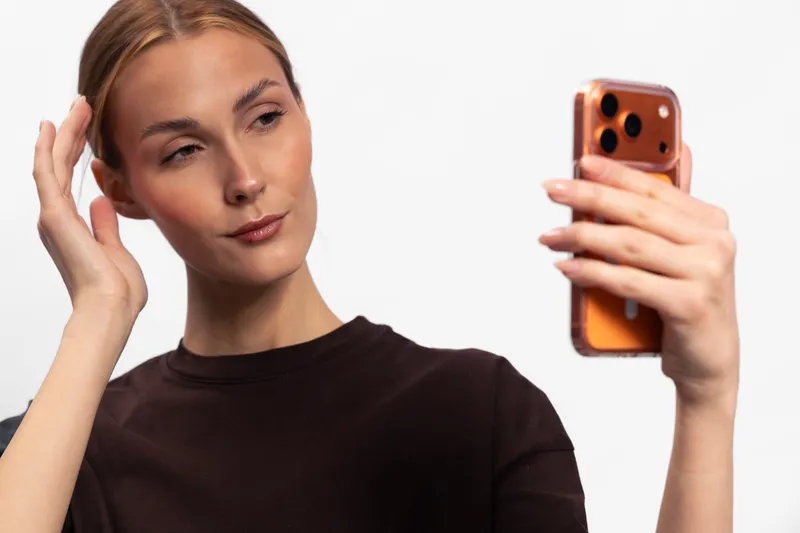 Young woman in black shirt takes a selfie with smartphone on white background. Concept for social media, technology, self portrait, and modern communication.