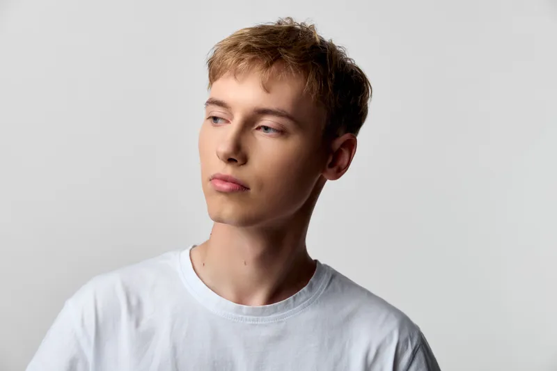Man, young, looking away, in a white t-shirt, photographed in a clean studio with soft lighting, conveying calm focus and a thoughtful mood for lifestyle, fashion, or editorial use.